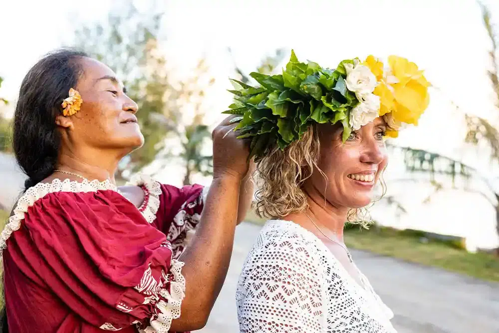 Polynesian woman placing flower crown on a smiling senior tourist